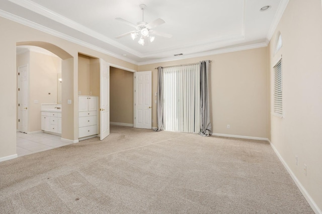 unfurnished bedroom featuring ceiling fan, ensuite bath, crown molding, a tray ceiling, and light carpet