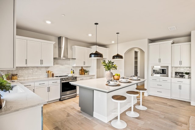 kitchen with appliances with stainless steel finishes, wall chimney exhaust hood, and white cabinetry