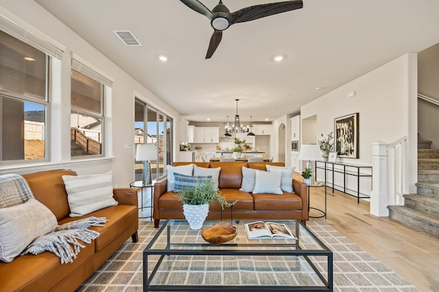 living room with ceiling fan with notable chandelier and light hardwood / wood-style flooring