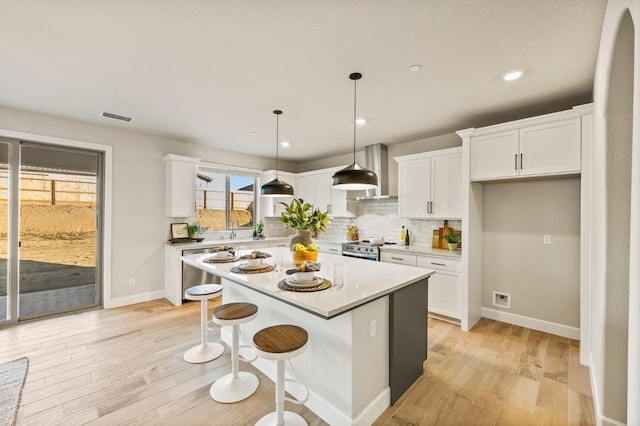 kitchen with pendant lighting, white cabinets, a kitchen island, backsplash, and light hardwood / wood-style flooring