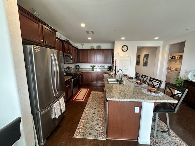 kitchen with dark hardwood / wood-style floors, sink, a kitchen island with sink, a kitchen breakfast bar, and stainless steel appliances