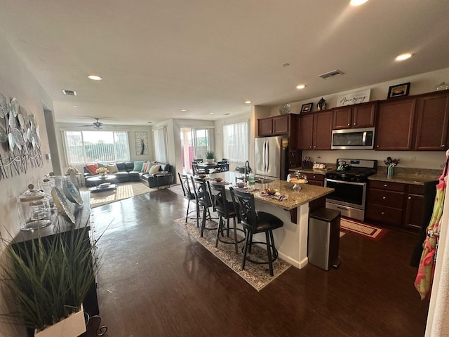 kitchen with appliances with stainless steel finishes, sink, a kitchen island with sink, light stone counters, and a breakfast bar area