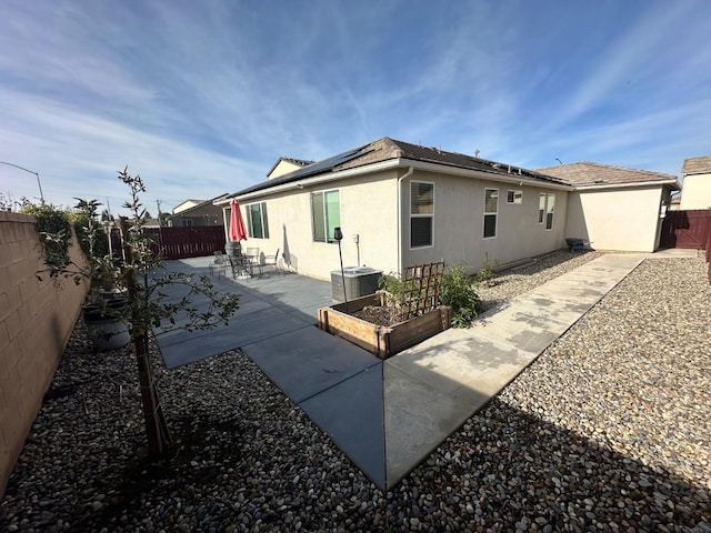 rear view of house featuring central AC unit, solar panels, and a patio