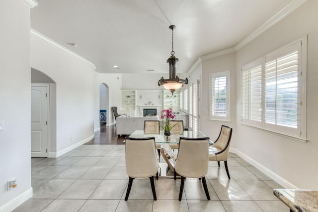 dining space featuring light tile patterned floors, a fireplace, arched walkways, and crown molding