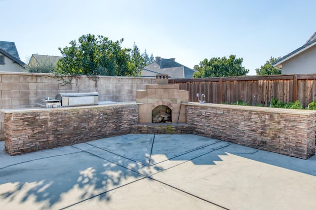 view of patio featuring fence, exterior kitchen, and an outdoor stone fireplace