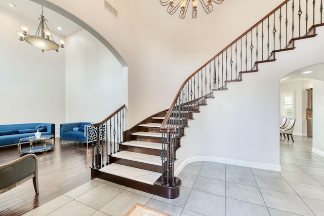 staircase featuring a high ceiling, baseboards, arched walkways, and a notable chandelier