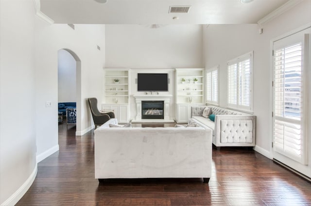 living room with visible vents, arched walkways, baseboards, a glass covered fireplace, and dark wood-style floors