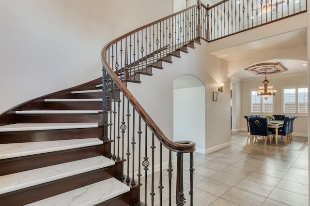 stairway featuring arched walkways, a high ceiling, baseboards, ornamental molding, and tile patterned floors