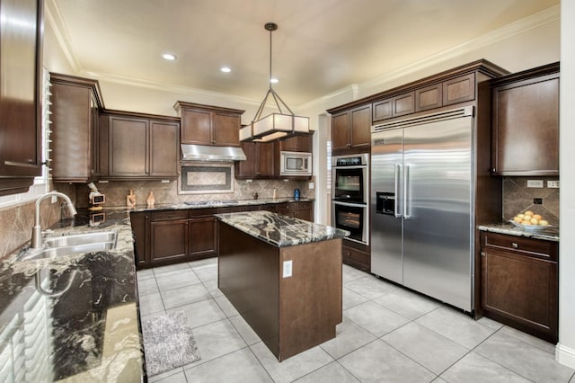 kitchen with ornamental molding, a sink, built in appliances, dark stone counters, and under cabinet range hood