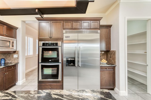 kitchen featuring ornamental molding, dark stone counters, and built in appliances