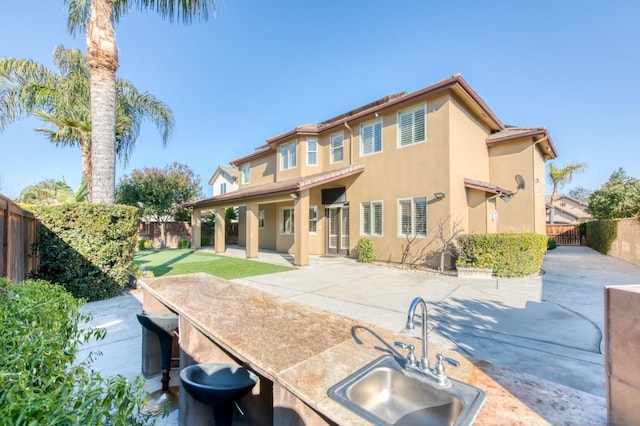 back of house with a sink, a fenced backyard, and stucco siding