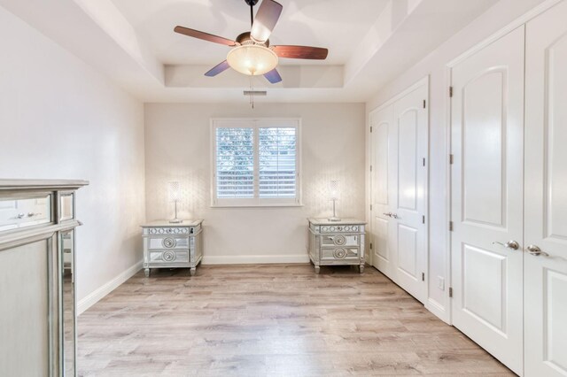 unfurnished bedroom with a raised ceiling, visible vents, ceiling fan, light wood-type flooring, and baseboards