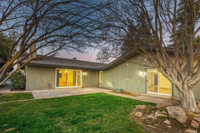 back house at dusk with a lawn and a patio