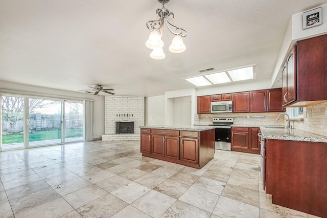 kitchen with appliances with stainless steel finishes, sink, a kitchen island, pendant lighting, and light stone counters