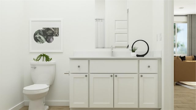 bathroom featuring baseboards, toilet, wood finished floors, and vanity