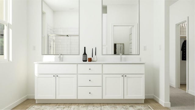 full bathroom with a shower stall, double vanity, baseboards, and a sink