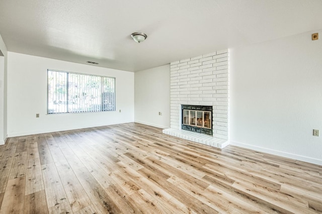 unfurnished living room with light wood-type flooring and a brick fireplace