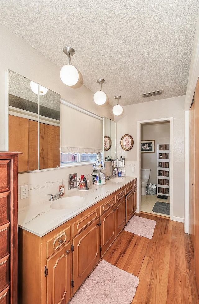 kitchen featuring sink, a textured ceiling, decorative light fixtures, and light hardwood / wood-style flooring