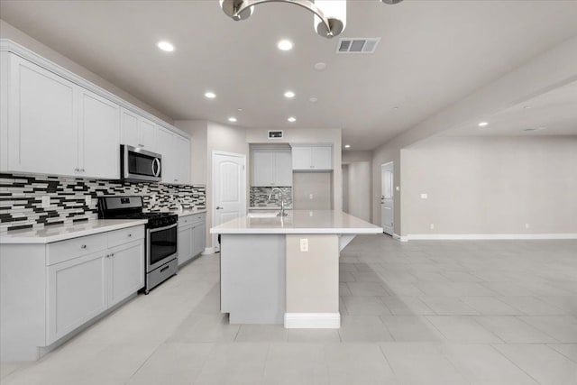 kitchen with sink, appliances with stainless steel finishes, an island with sink, white cabinets, and backsplash