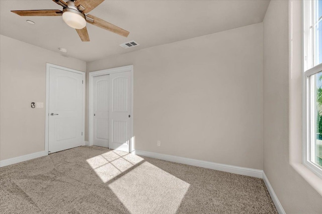 unfurnished bedroom with multiple windows, light colored carpet, ceiling fan, and a closet