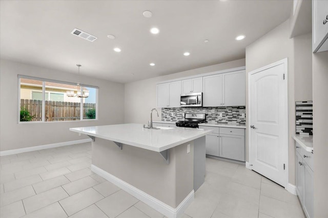 kitchen with decorative light fixtures, sink, decorative backsplash, stainless steel appliances, and a center island with sink