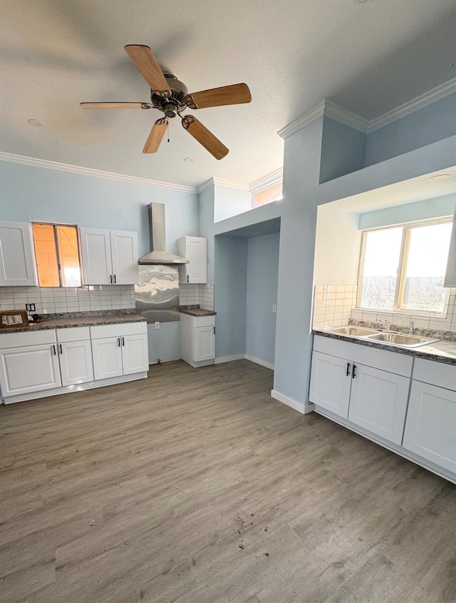 kitchen featuring a sink, white cabinetry, crown molding, and wall chimney range hood