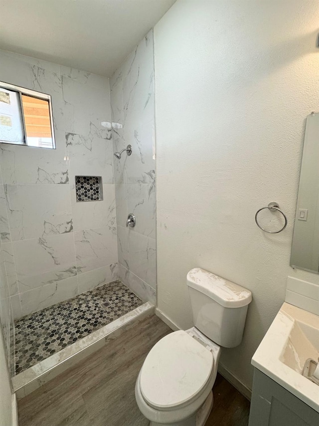 bathroom featuring vanity, wood finished floors, baseboards, tiled shower, and toilet