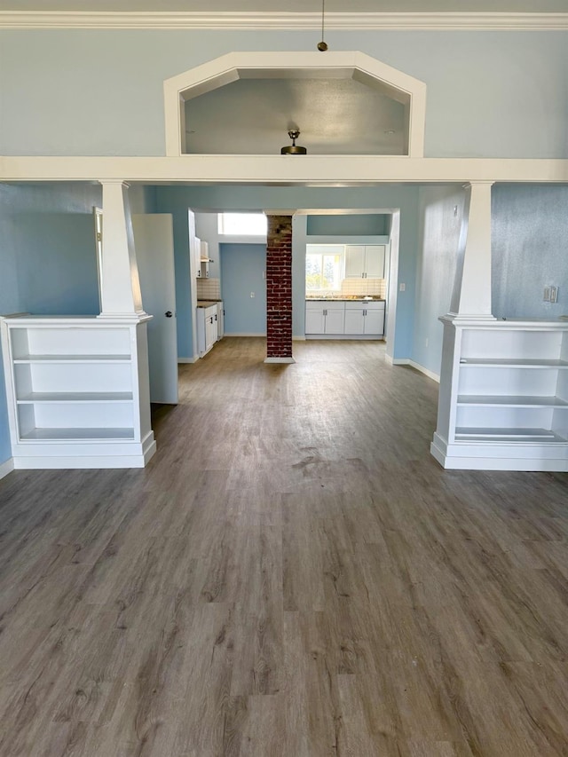 unfurnished living room featuring baseboards, crown molding, ornate columns, and wood finished floors