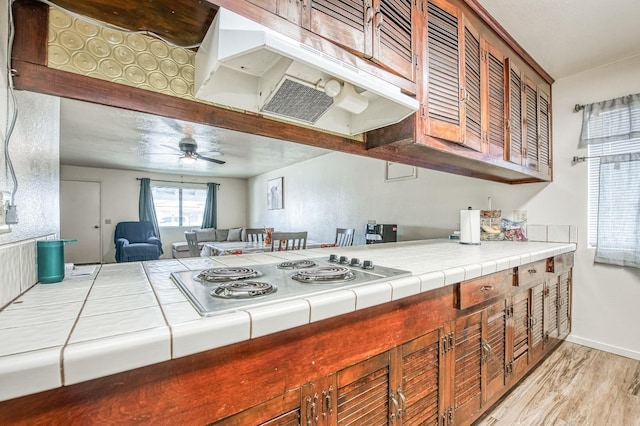 kitchen with tile counters, stovetop, ceiling fan, and light wood-type flooring