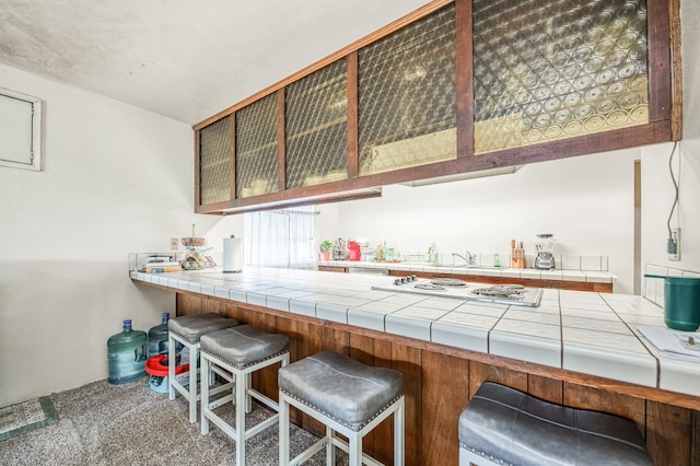 kitchen featuring white cooktop, tile counters, a kitchen breakfast bar, and carpet