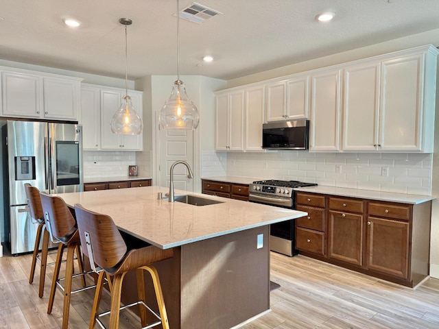 kitchen featuring appliances with stainless steel finishes, a kitchen island with sink, sink, and white cabinets