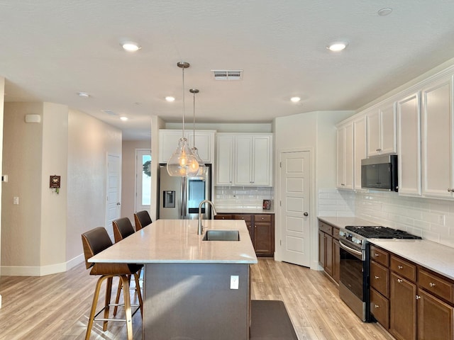 kitchen with pendant lighting, sink, white cabinets, stainless steel appliances, and a center island with sink