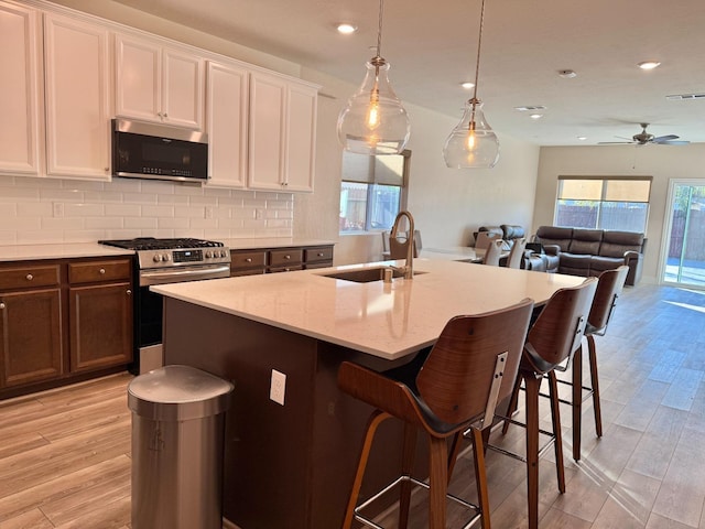 kitchen featuring pendant lighting, stainless steel appliances, a kitchen island with sink, and white cabinets