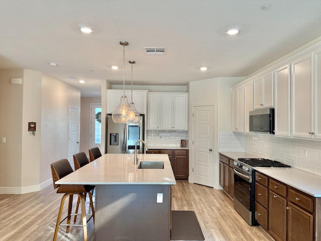 kitchen with sink, a center island with sink, a kitchen breakfast bar, stainless steel appliances, and white cabinets