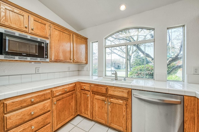 kitchen featuring vaulted ceiling, dishwasher, sink, black microwave, and tile counters