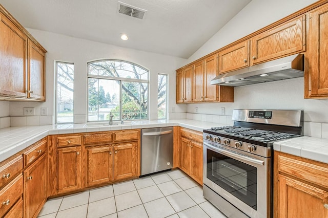 kitchen with vaulted ceiling, sink, stainless steel appliances, light tile patterned floors, and tile counters