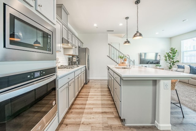 kitchen featuring stainless steel appliances, a kitchen breakfast bar, backsplash, gray cabinets, and light hardwood / wood-style flooring