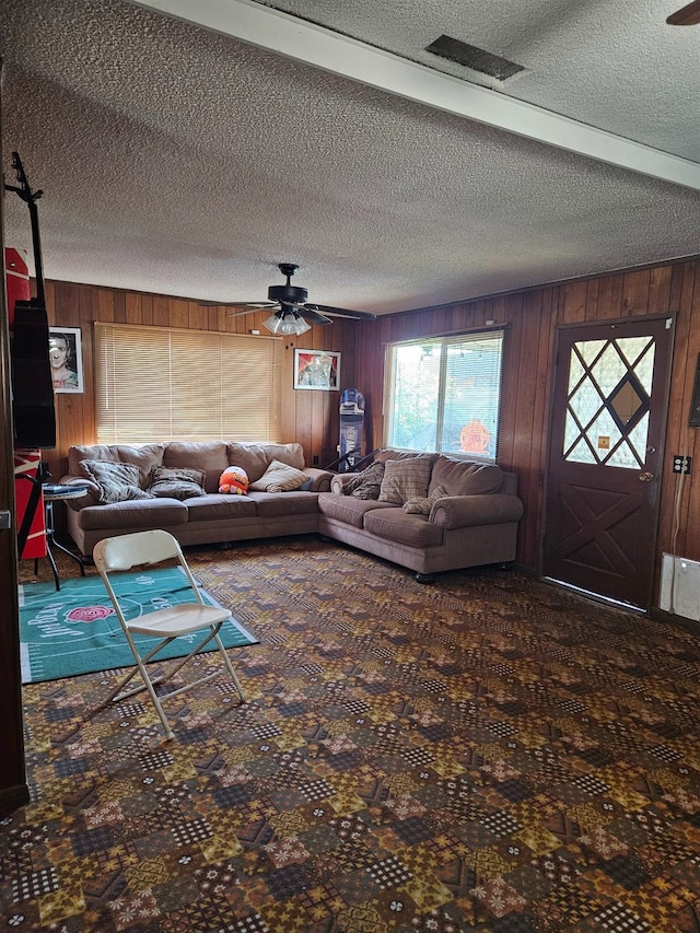 carpeted living room featuring ceiling fan, a textured ceiling, and wood walls