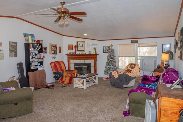 carpeted living room featuring vaulted ceiling, ceiling fan, a tiled fireplace, a textured ceiling, and ornamental molding