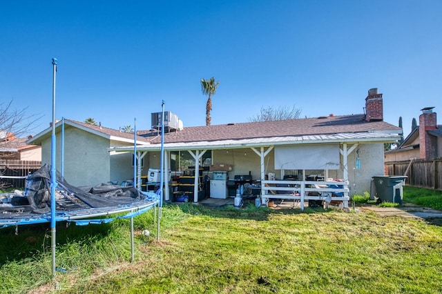 back of house featuring a yard, a trampoline, and central AC unit