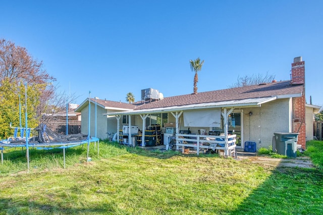 rear view of house with a yard, a trampoline, and central AC