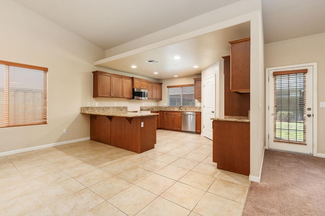 kitchen with light stone countertops, appliances with stainless steel finishes, light carpet, kitchen peninsula, and a breakfast bar area