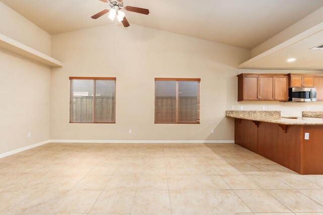 kitchen with lofted ceiling, light tile patterned flooring, ceiling fan, and light stone countertops