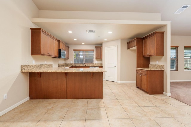 kitchen featuring light stone counters, plenty of natural light, light tile patterned floors, and kitchen peninsula