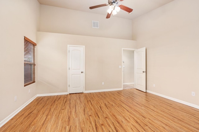 unfurnished bedroom with light wood-type flooring, ceiling fan, and a high ceiling