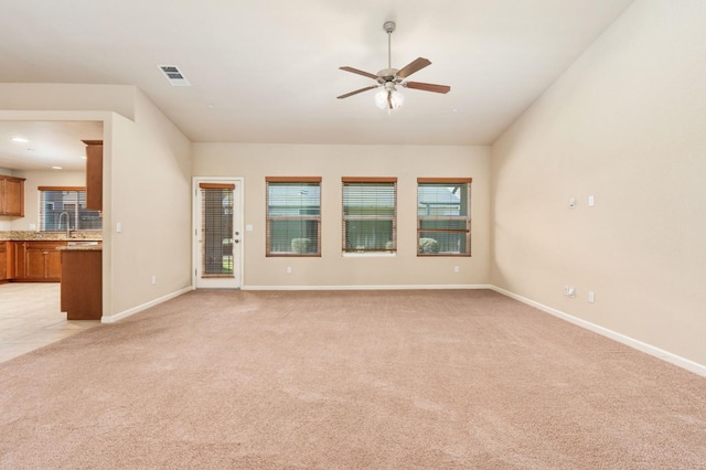 unfurnished living room featuring ceiling fan, light colored carpet, and sink