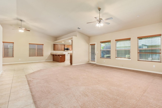 unfurnished living room featuring ceiling fan, a wealth of natural light, light tile patterned floors, and vaulted ceiling