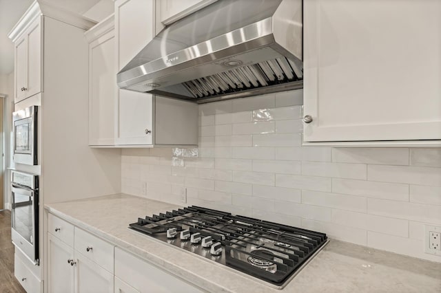 kitchen featuring tasteful backsplash, white cabinetry, exhaust hood, stainless steel appliances, and light stone countertops