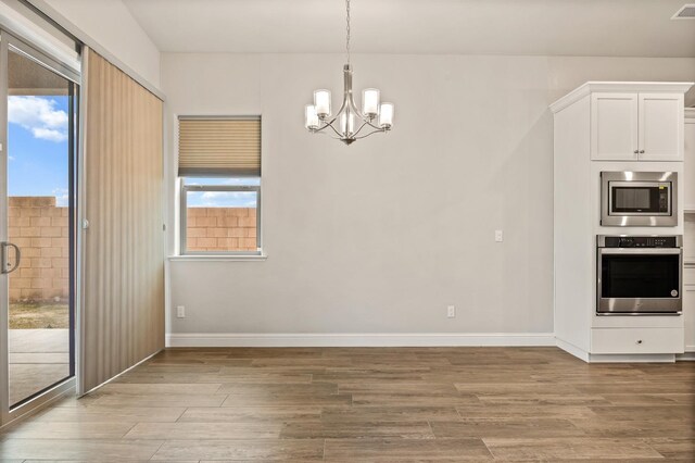 kitchen featuring white cabinets, hanging light fixtures, a notable chandelier, stainless steel appliances, and light wood-type flooring