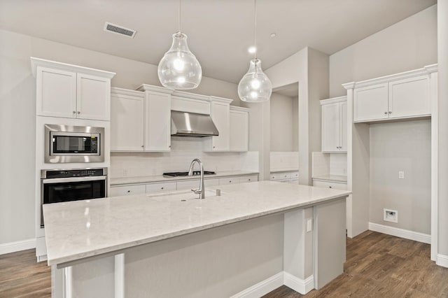 kitchen featuring pendant lighting, white cabinetry, stainless steel appliances, light stone countertops, and wall chimney range hood